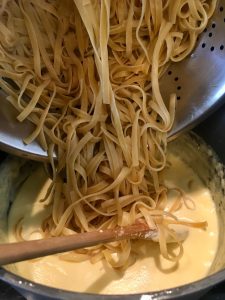 Photo of adding cooked pasta to the Alfredo sauce.