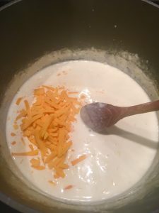 Photo of mixing cheddar cheese into cream sauce.
