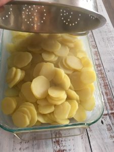 Photo of pouring potatoes in buttered dish.