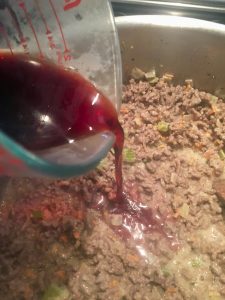 Photo of adding wine to bolognese meat sauce.