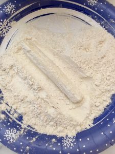 Photo of rolling mozzarella stick in flour. 