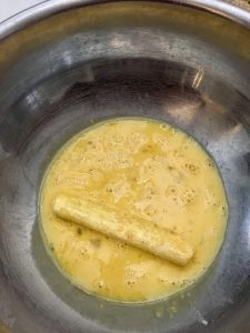 Photo of rolling mozzarella stick in egg mixture. 