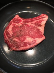 Photo of raw rib eye steak in a pan.