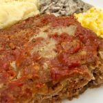 Photo of meatloaf served with a generous portion of mashed potatoes, mushroom gravy, and creamed corn.