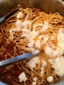 Photo of stirring parmesan cheese into pasta and meat sauce.