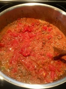 Photo of adding diced and pureed tomatoes to bolognese meat sauce.