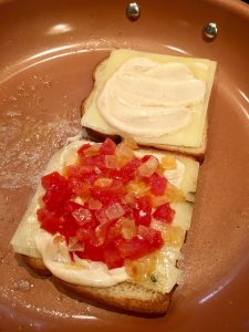 Photo of onion and tomatoes on top of open faced sandwich.
