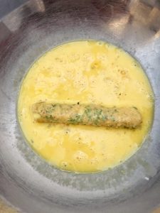 Photo of re-rolling mozzarella stick in egg mixture. 