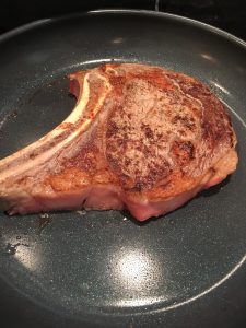Photo of rib eye steak cooking in pan.