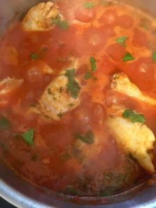 Chicken cooking in chicken stock and tomato sauce. 