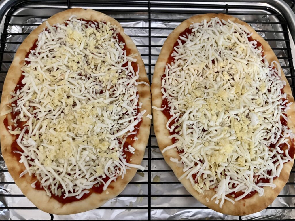 Add shredded cheeses to flatbreads. 