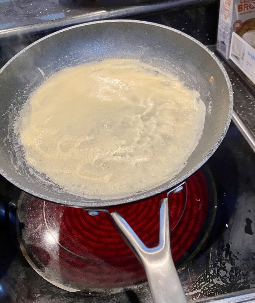 Lift the pan a few inches off the heat.  Pour about 1/4 to 1/3 cup of the crepe batter in the pan starting on one side and rotating the pan to spread the batter.