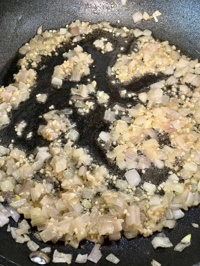 Onions, shallots, and garlic cooking in a pan. 