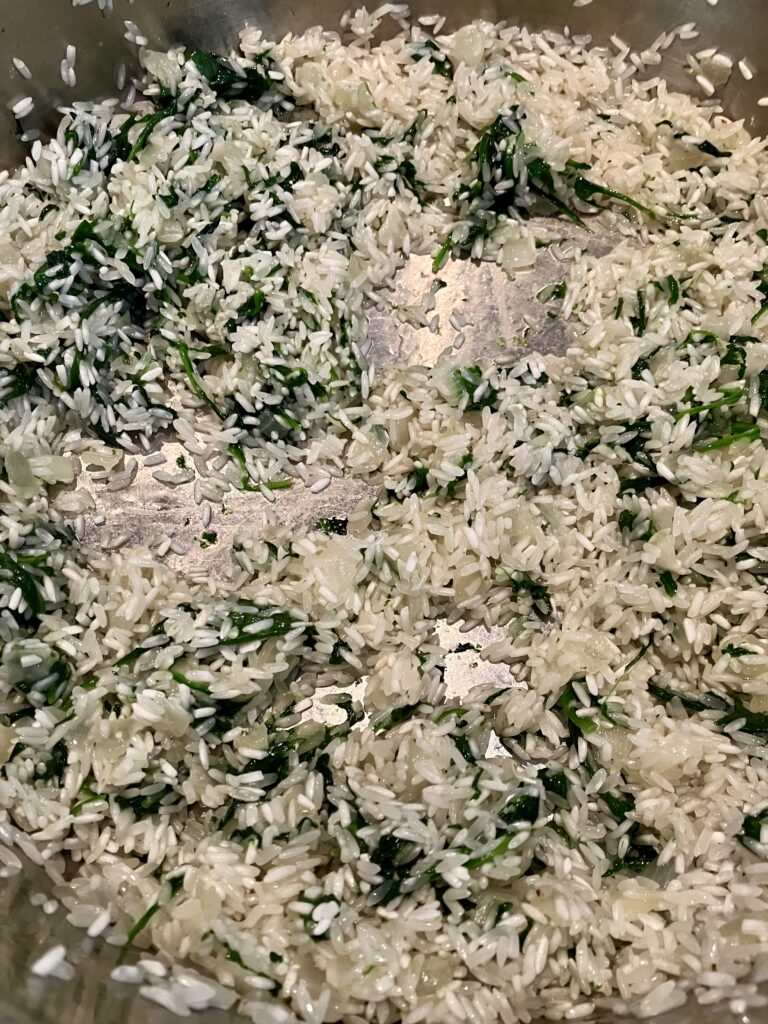 Rice toasting in a pan with spinach and onions. 