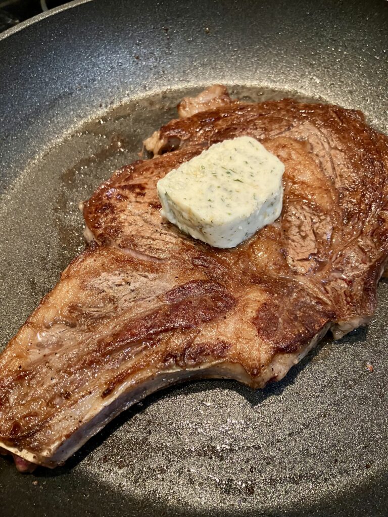 Photo of steak in a pan with Garlic Butter for Steak. 