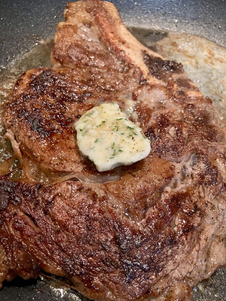 Photo of a steak in a pan with Garlic Herb Butter for Steak.